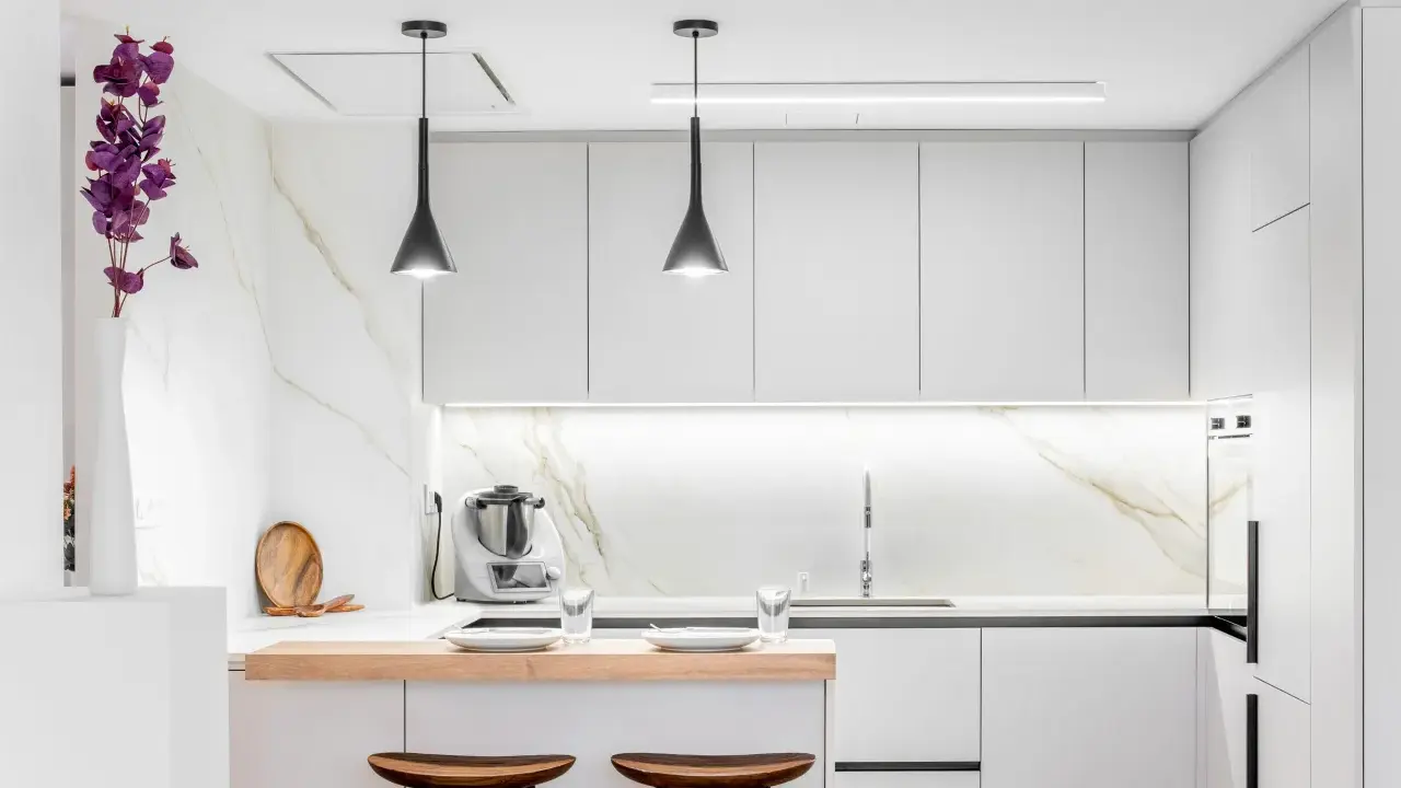 Moderna cocina pequeña con encimeras de mármol, gabinetes blancos y una barra de desayuno de madera.