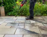 Persona con guantes rojos usa hidrolimpiadora para limpiar el suelo de la terraza, dejando las baldosas relucientes.