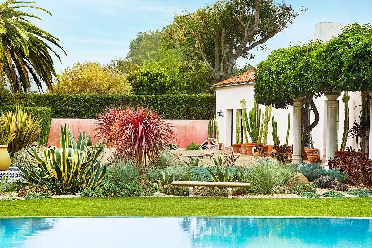 Fachadas de casas de estilo mediterráneo con exuberante jardín desértico, piscina y palmeras.