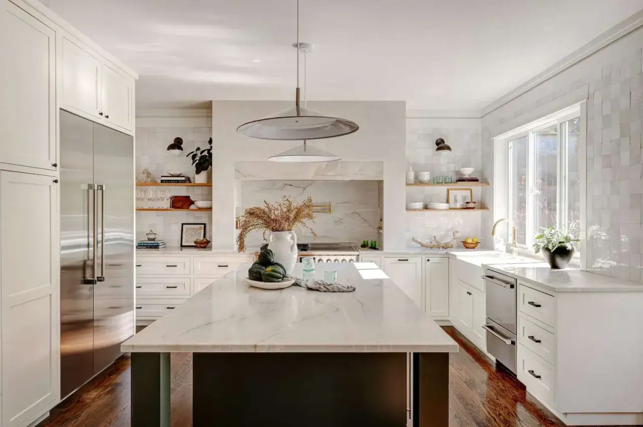 Elegante cocina pequeña con isla central de mármol, electrodomésticos de acero inoxidable y azulejos blancos.