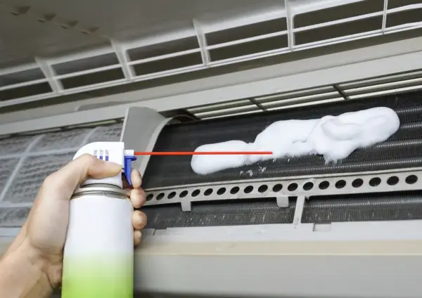Mano rociando espuma para limpiar aire acondicionado unidad interior.