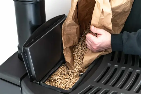 Persona rellena el depósito de una estufa de pellets con combustible.