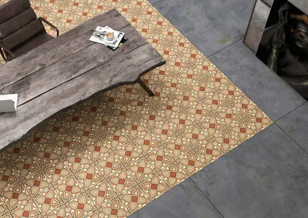 Un suelo hidráulico con diseño geométrico en tonos tierra y ocre, junto a un suelo de cemento pulido. Una mesa de madera rústica y una silla completan la escena.