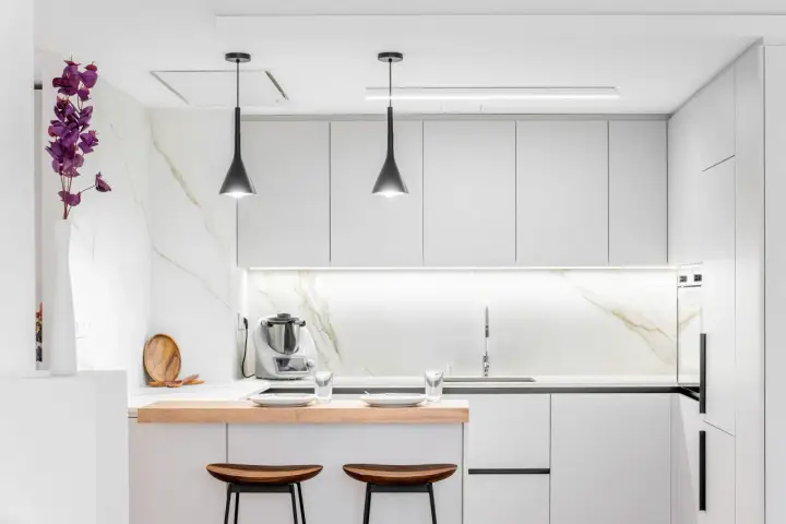 Moderna cocina pequeña con encimeras de mármol, gabinetes blancos y una barra de desayuno de madera.
